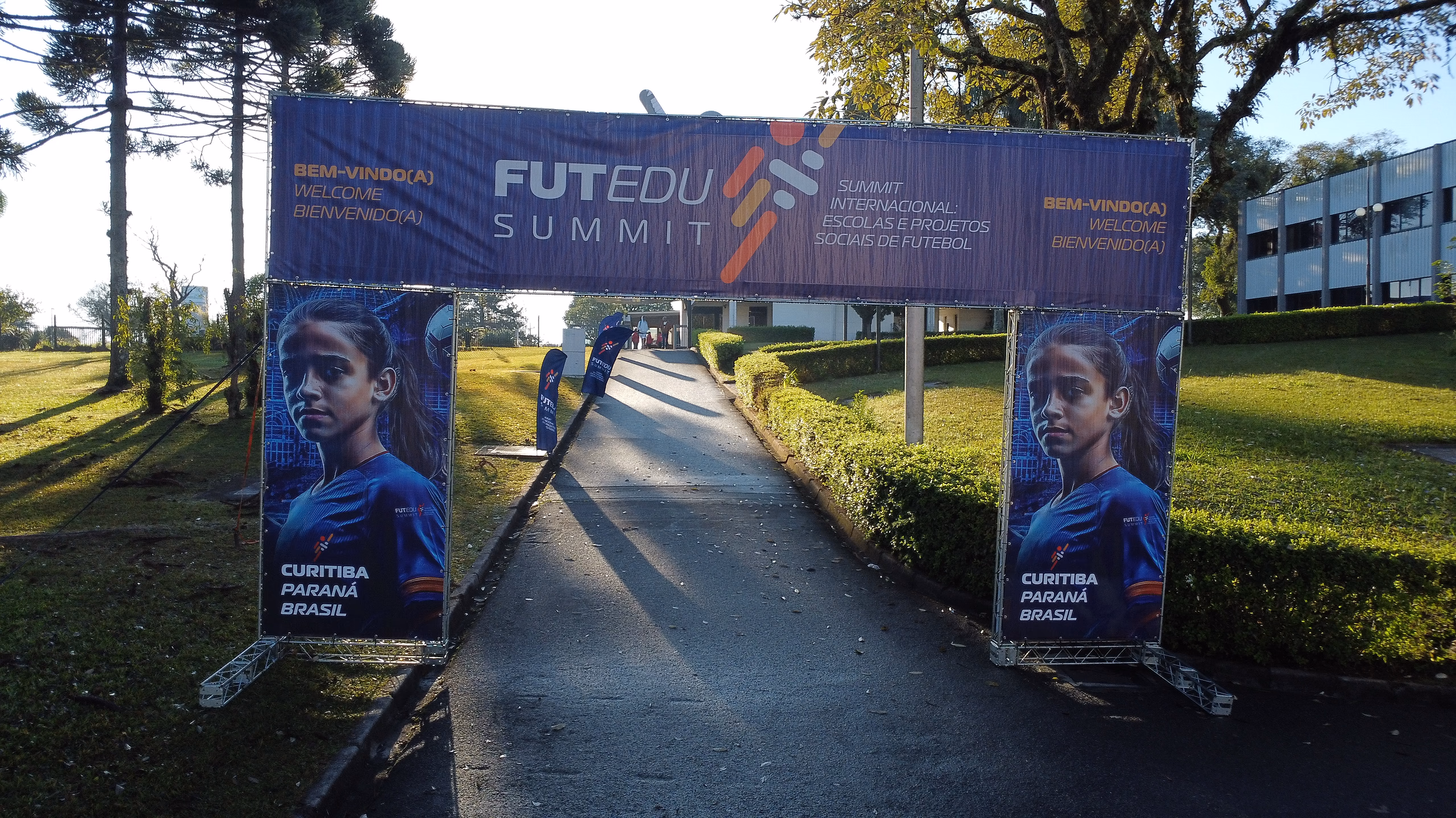 Pórtico de boas-vindas do FutEdu Summit sobre a alameda de entrada, em Curitiba.