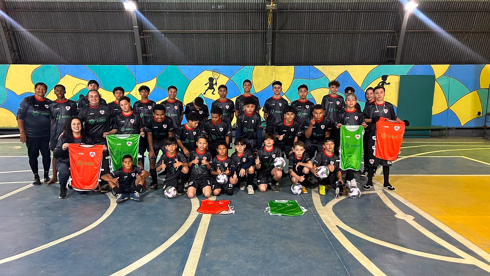 Turma do Futsal na Escola reunida na quadra coberta, com os coletes e as bolas do projeto.
