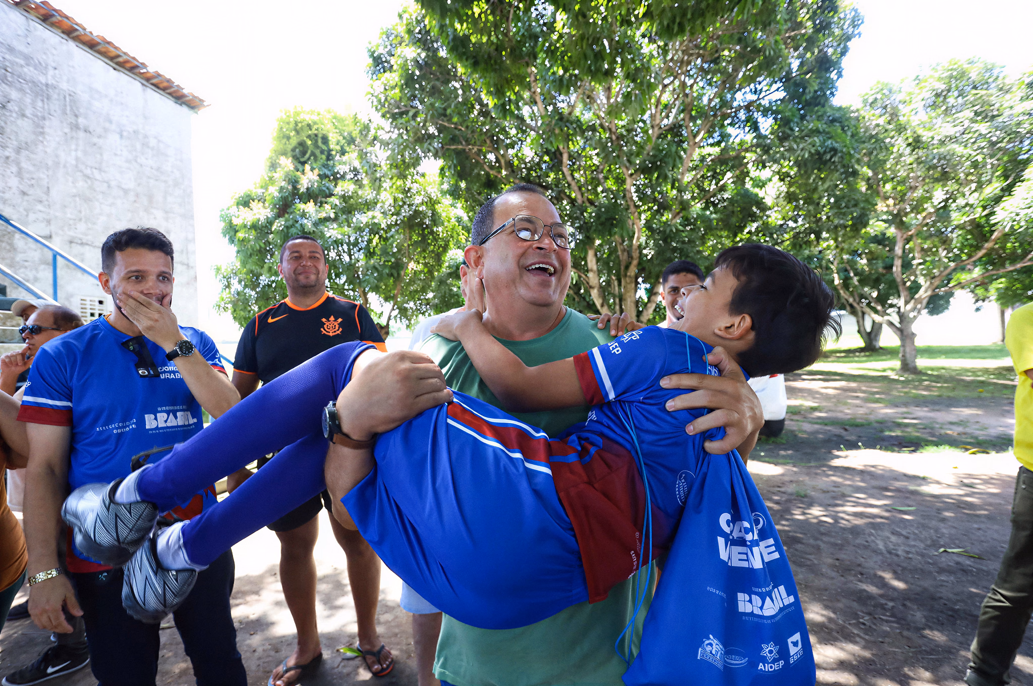 Professor carrega no colo um menino que ri, cercado pela turma, no dia do polo de Estância.